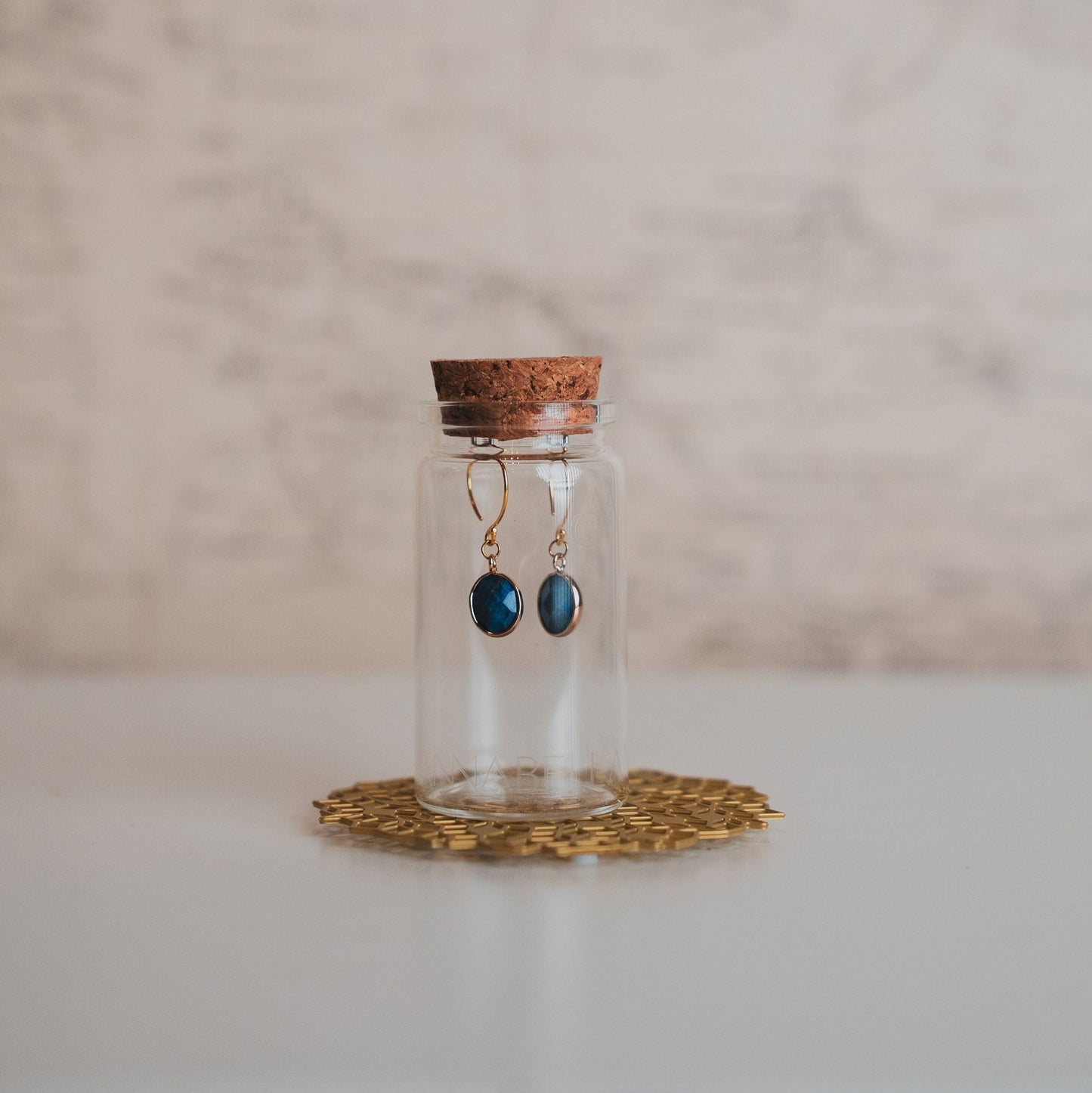 Glass bottle with cork lid containing earrings on a textured surface
