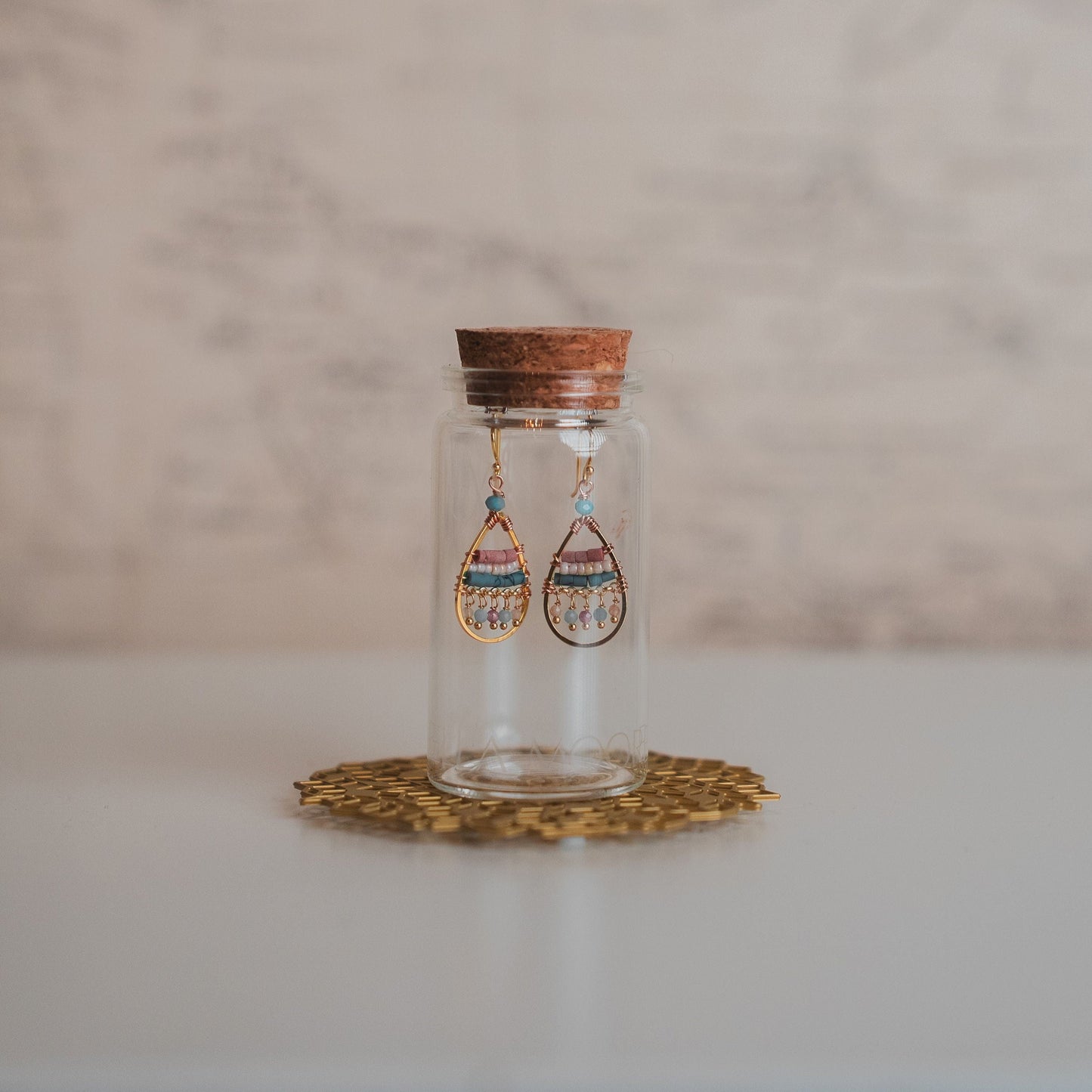 Glass jar with wooden lid containing earrings on a marble surface