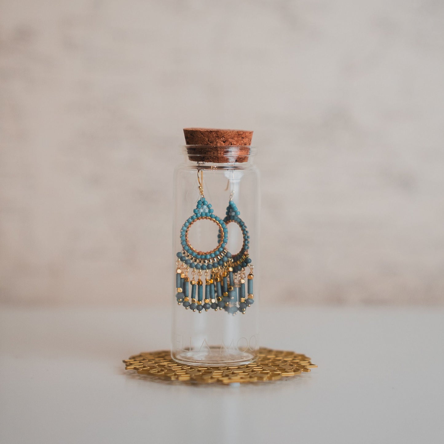 Decorative earrings in a glass bottle with cork lid on a white surface.