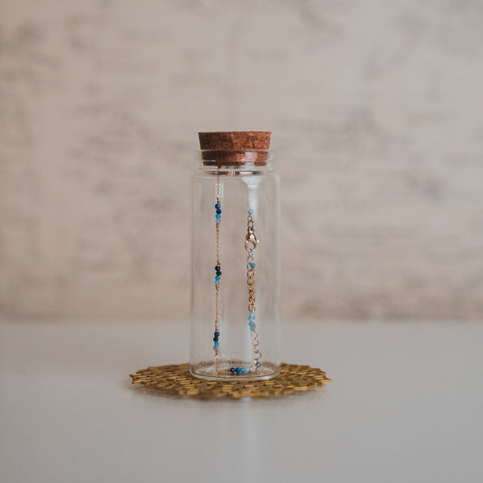 Glass bottle with cork lid containing beaded necklaces on a marble surface