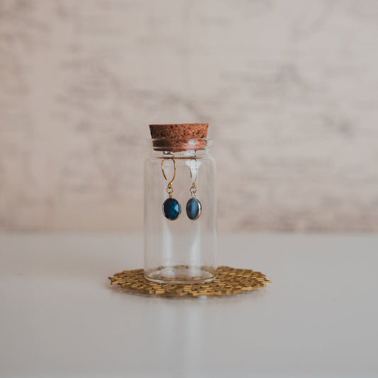 Glass bottle with cork lid containing earrings on a textured surface