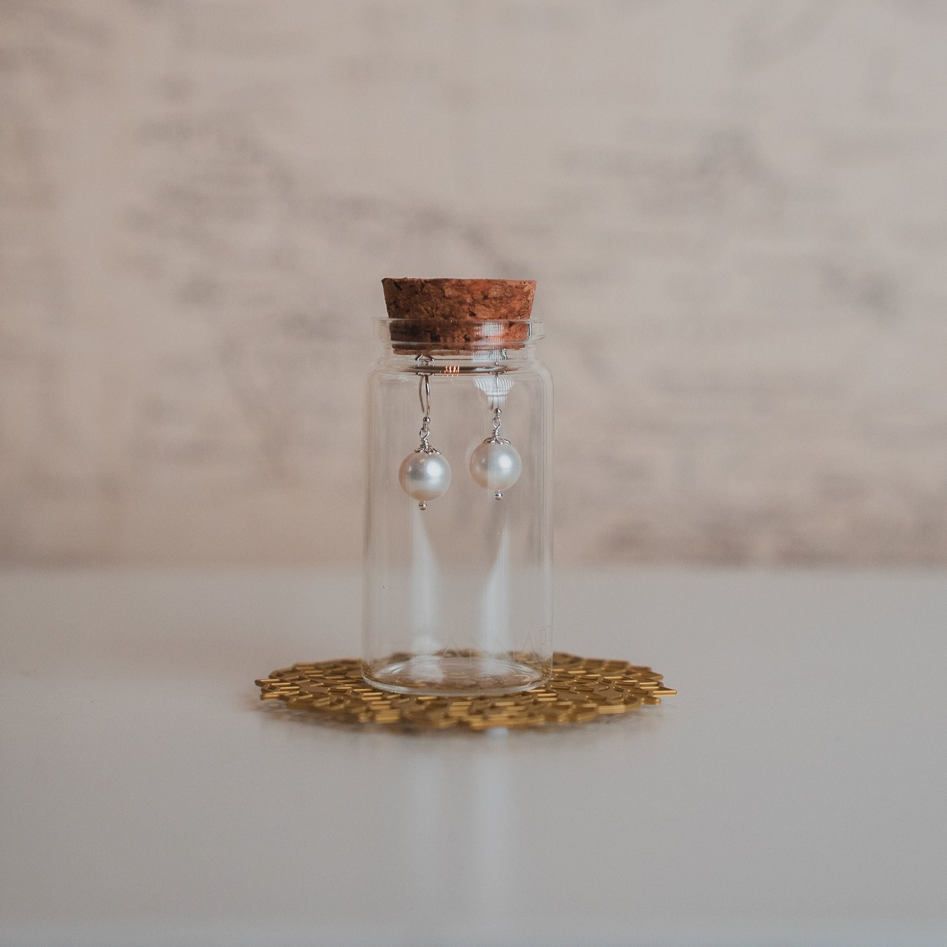 Glass bottle with cork lid containing a pair of earrings on a marble surface