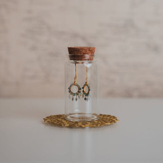 Glass bottle with cork lid containing earrings on a textured surface