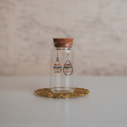 Glass jar with wooden lid containing earrings on a marble surface