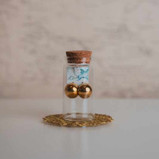 Small glass bottle with cork lid containing gold balls on a decorative coaster with a marble background