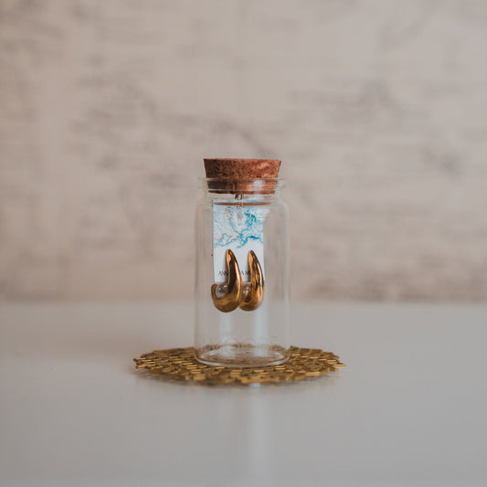 Small glass jar with a cork lid containing gold shoes on a marble surface.